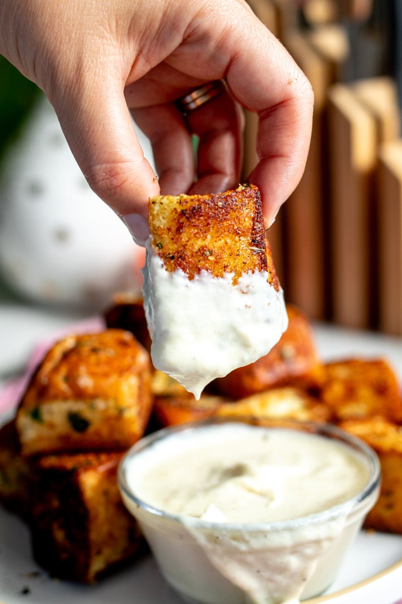 a hand holding a hawaiian roll garlic bread being dunked into a creamy white alfredo sauce. 