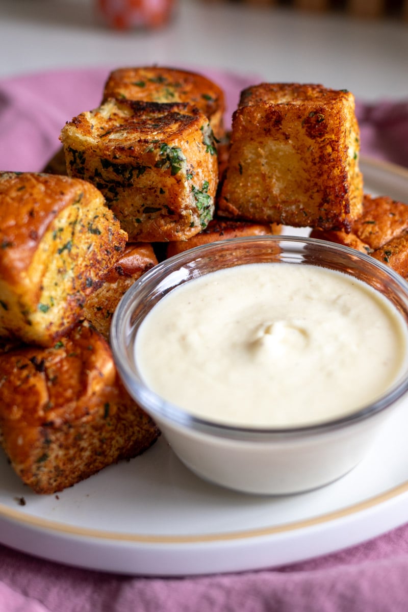 a plate with hawaiian roll garlic bread bites on it and some white cream sauce to dip. 