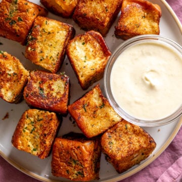 hawaiian roll garlic bread on a white plate with white cream sauce dip.