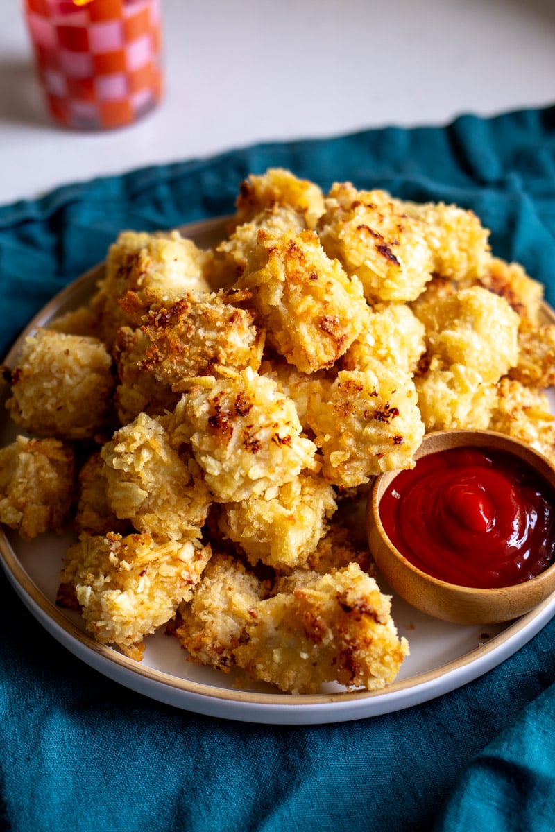 a white plate full of crispy golden popcorn chicken nuggets and ketchup dip.