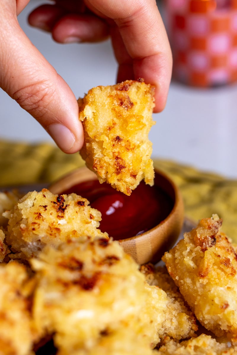 a hand holding a piece of popcorn chicken dipping it into ketchup.
