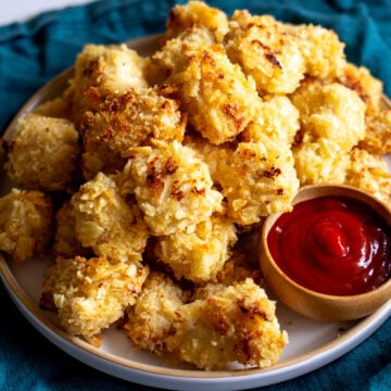 a white plate full of crispy golden popcorn chicken nuggets and ketchup dip.