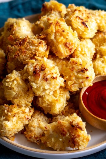 a white plate full of crispy golden popcorn chicken nuggets and ketchup dip.