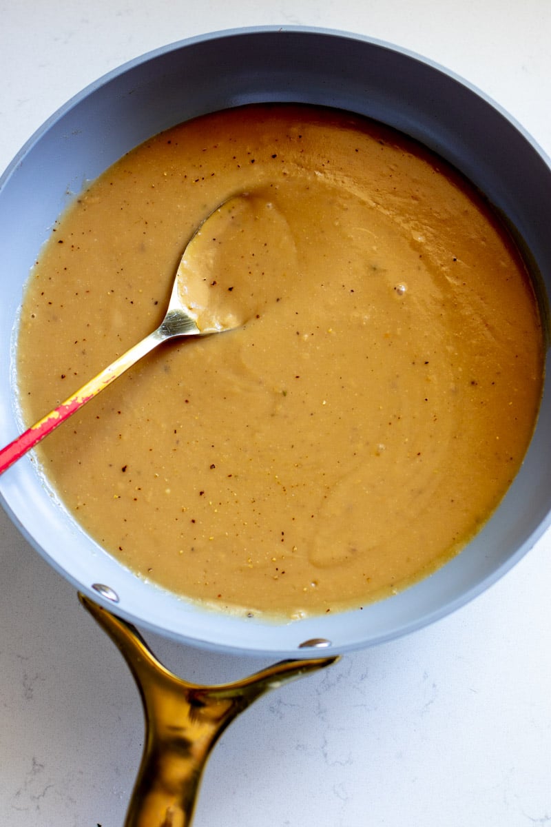 an overhead view of a saute pan on a white countertop with a golden spoon in it. 
