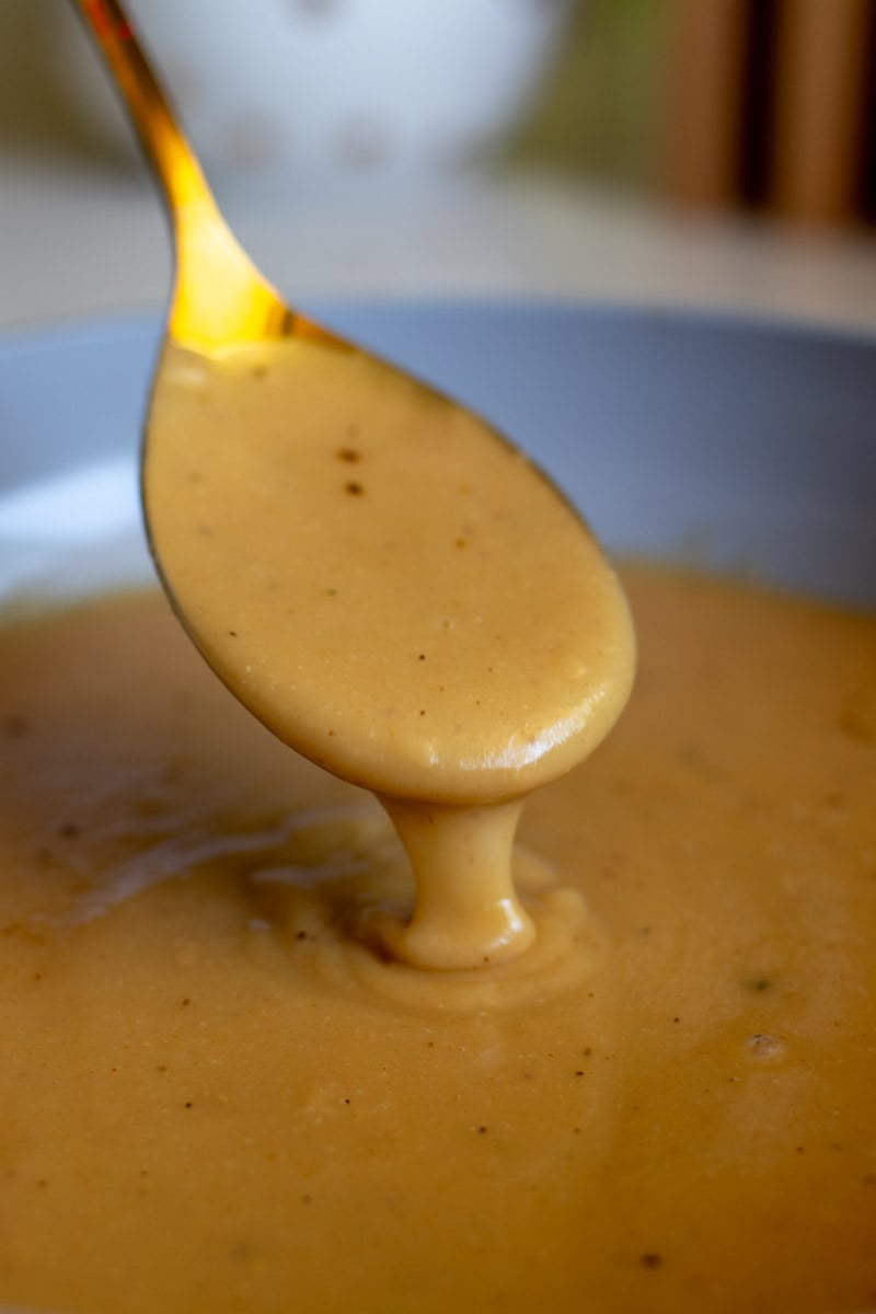a golden spoon pouring golden brown chicken gravy that's made from broth in a sauce pan.