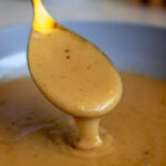 a golden spoon pouring golden brown chicken gravy that's made from broth in a sauce pan.