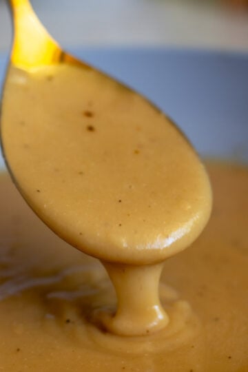 a golden spoon pouring golden brown chicken gravy that's made from broth in a sauce pan.