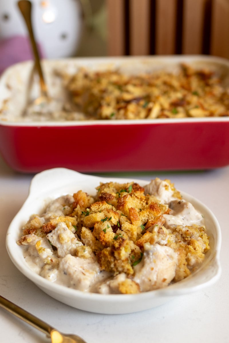 stove top stuffing and chicken casserole in a small cream colored bowl with a serving dish behind it.