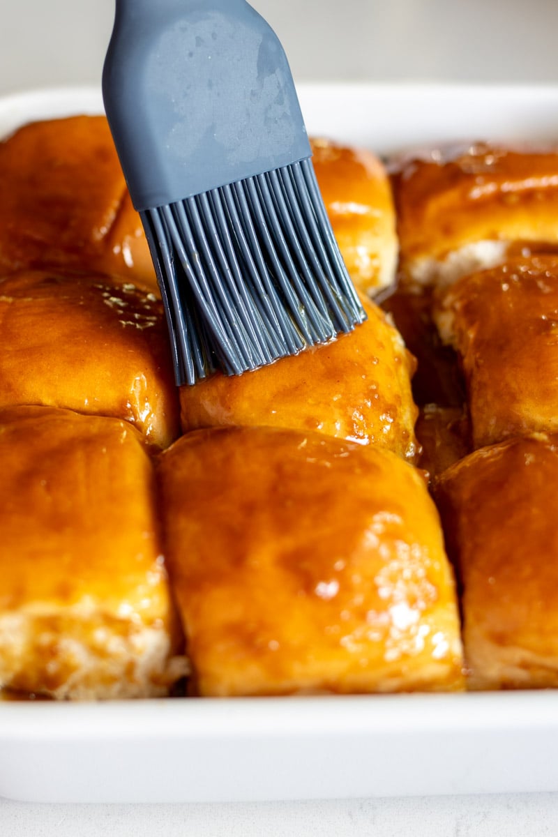 sauce being brushed onto hawaiian rolls before being baked.