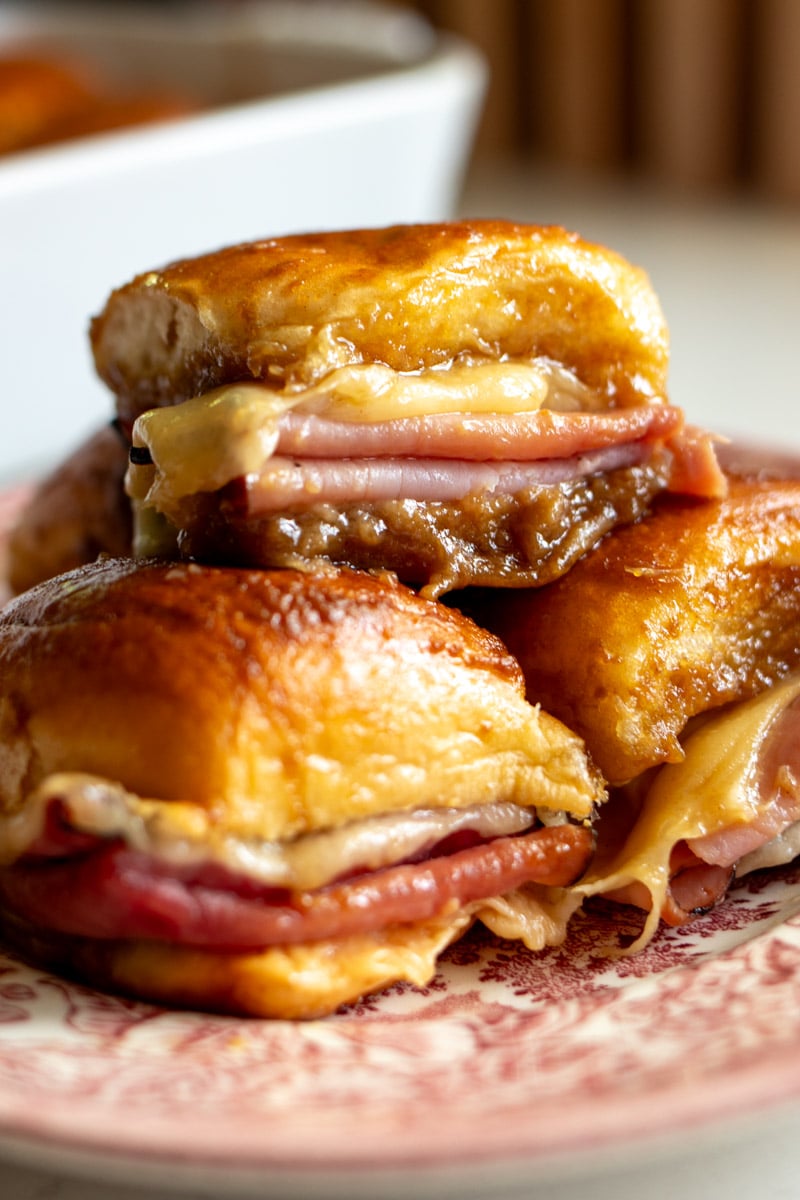 three funeral sandwiches loaded with melty swiss, savory ham and a beautiful golden butter glaze made of brown sugar, Worcestershire and dijon mustard on a pink plate.