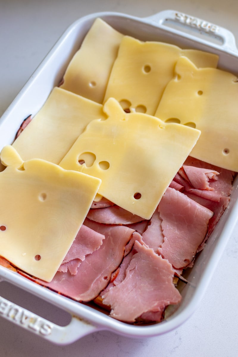 ham and swiss on top of hawaiian rolls in a baking dish. 
