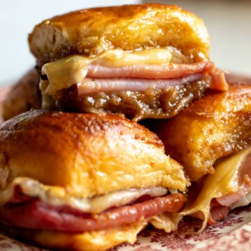 three funeral sandwiches loaded with melty swiss, savory ham and a beautiful golden butter glaze made of brown sugar, Worcestershire and dijon mustard on a pink plate.