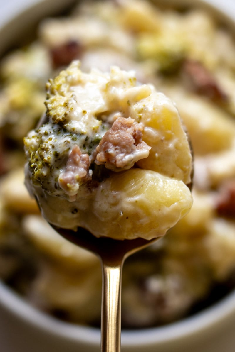 a spoon holding a scoop of broccoli sausage feta gnocchi.