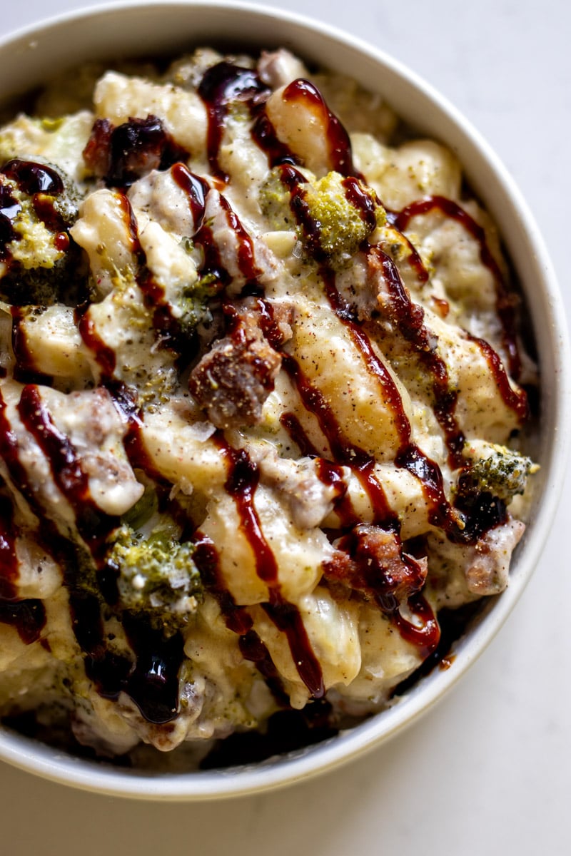 a white bowl full of a creamy broccoli sausage gnocchi recipe with a drizzle of balsamic glaze.