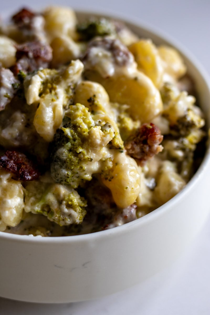 a white bowl topped with creamy feta sausage and broccoli pasta.
