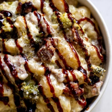 a white bowl full of a creamy broccoli sausage gnocchi recipe with a drizzle of balsamic glaze.
