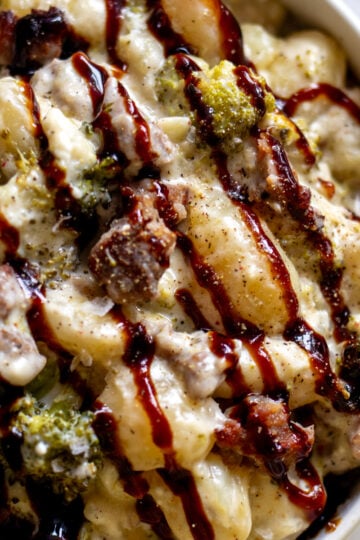 a white bowl full of a creamy broccoli sausage gnocchi recipe with a drizzle of balsamic glaze.