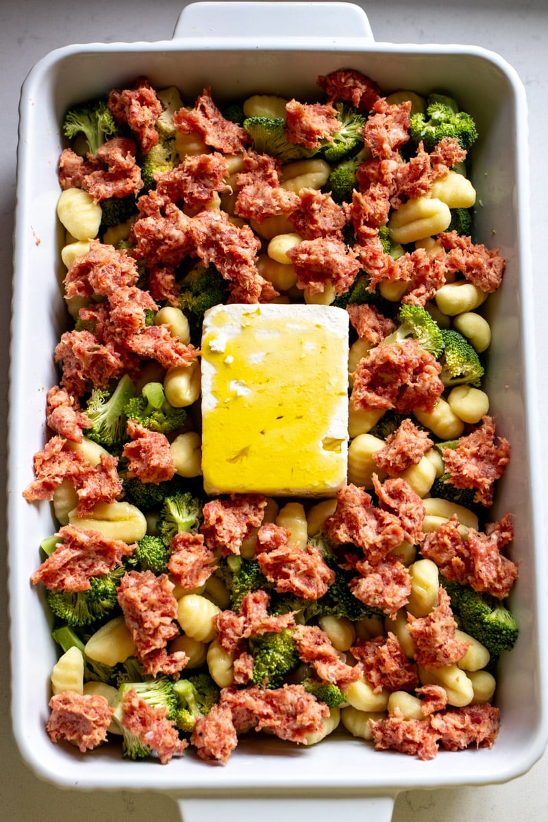 a baking dish filled with broccoli, sausage, and feta cheese.