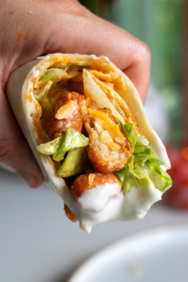 a hand holding half of a buffalo chicken pizza wrap after dunking it into ranch dressing.