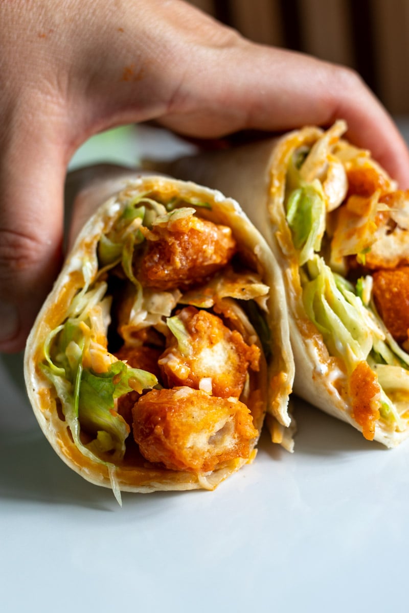 a hand holding two halves of a buffalo chicken pizza wrap on a white plate. 