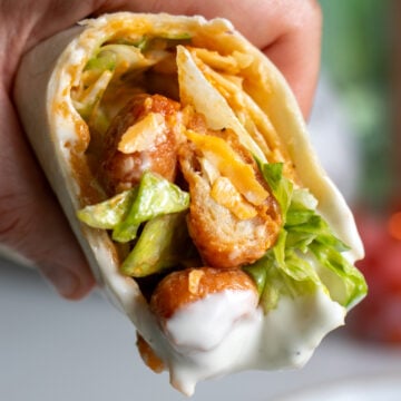 a hand holding half of a buffalo chicken pizza wrap after dunking it into ranch dressing.