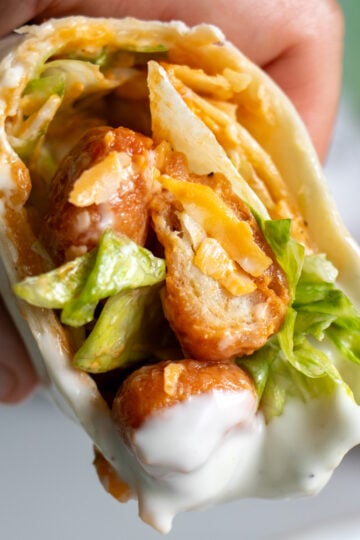 a hand holding half of a buffalo chicken pizza wrap after dunking it into ranch dressing.