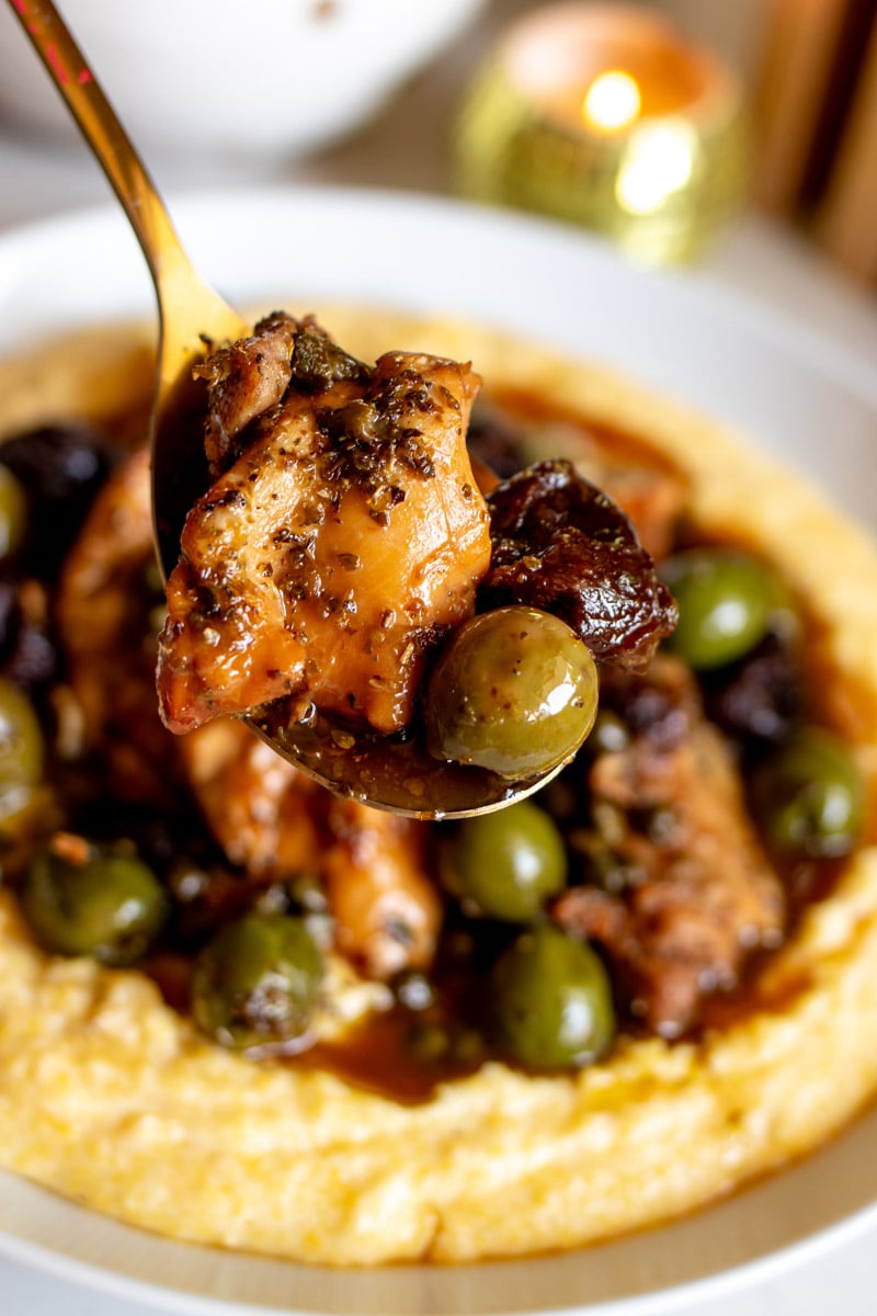 a golden spoon holding a scoop of chicken marbella over the serving bowl.
