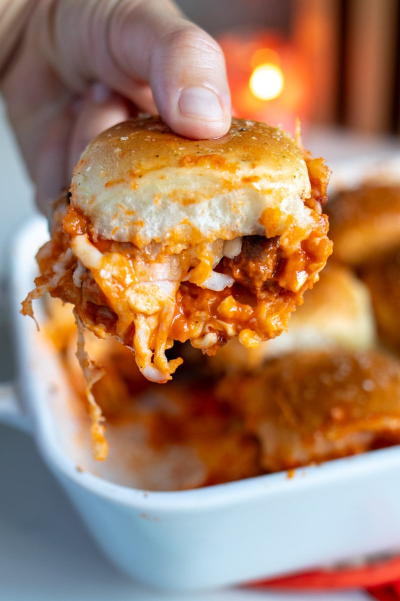 a hand holding a singular chicken parm slider with cheese and vodka sauce oozing out.