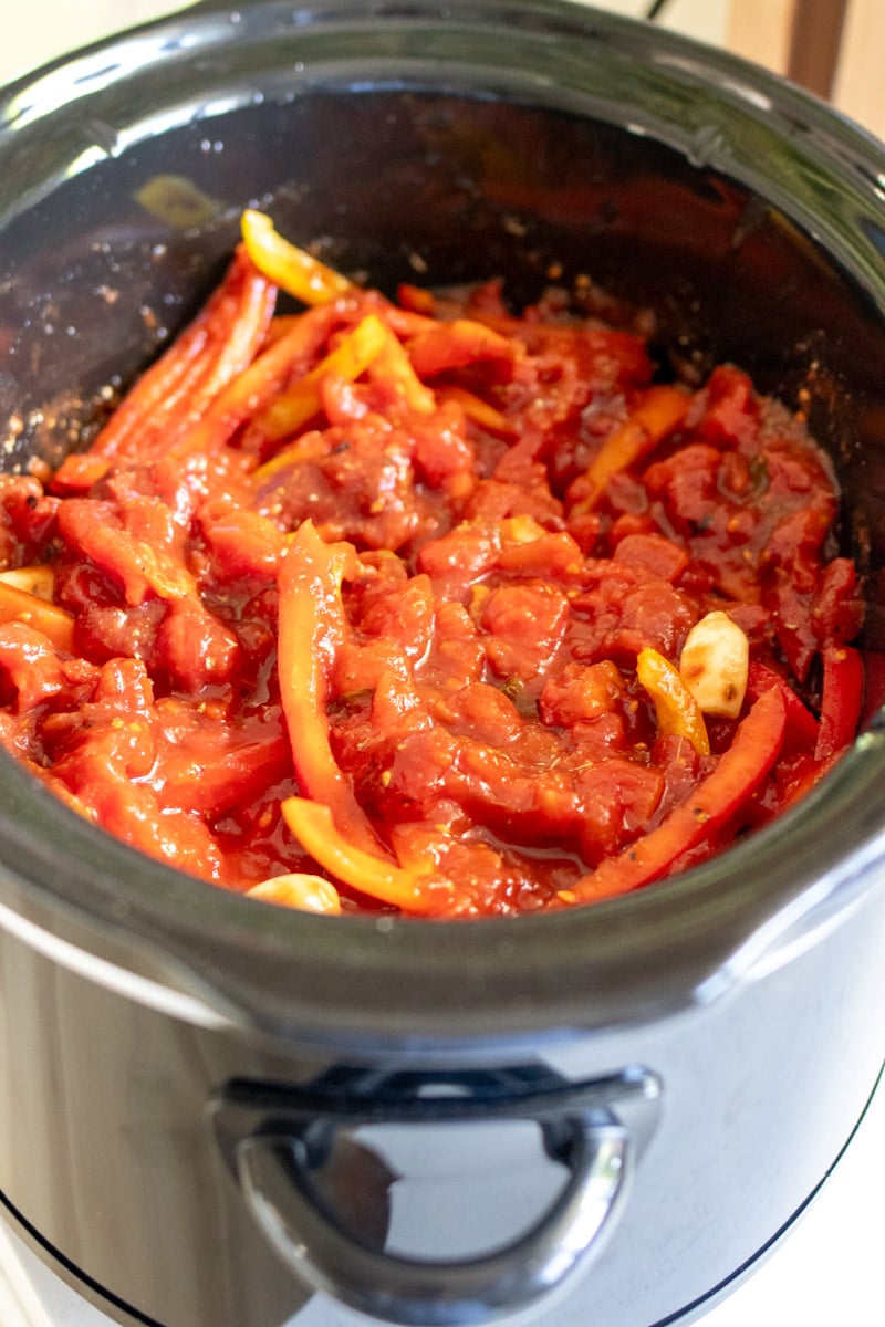 a black crockpot filled with sausage, peppers, onions and tomato sauce with spices. 