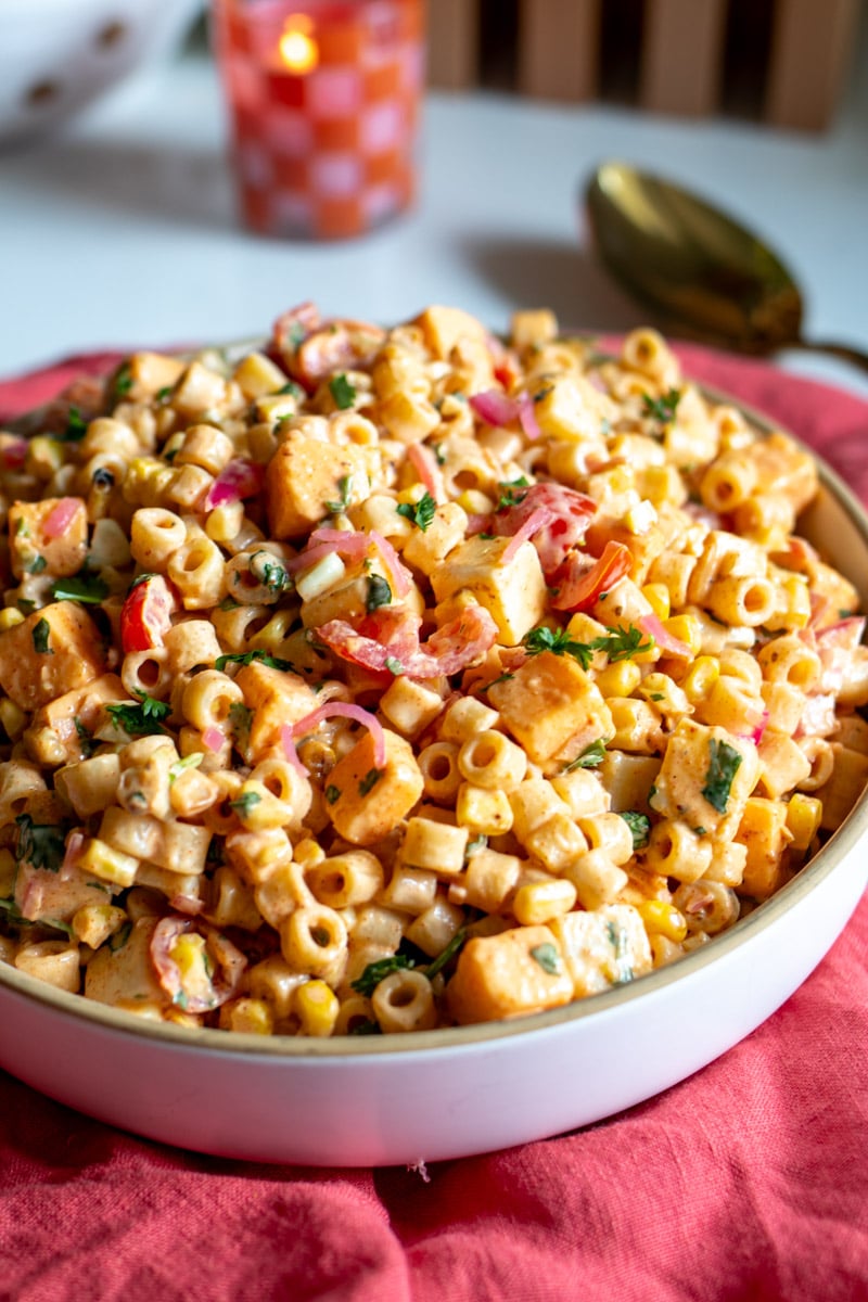 a white bowl full of zesty mexican street corn elote pasta salad on a pink napkin.