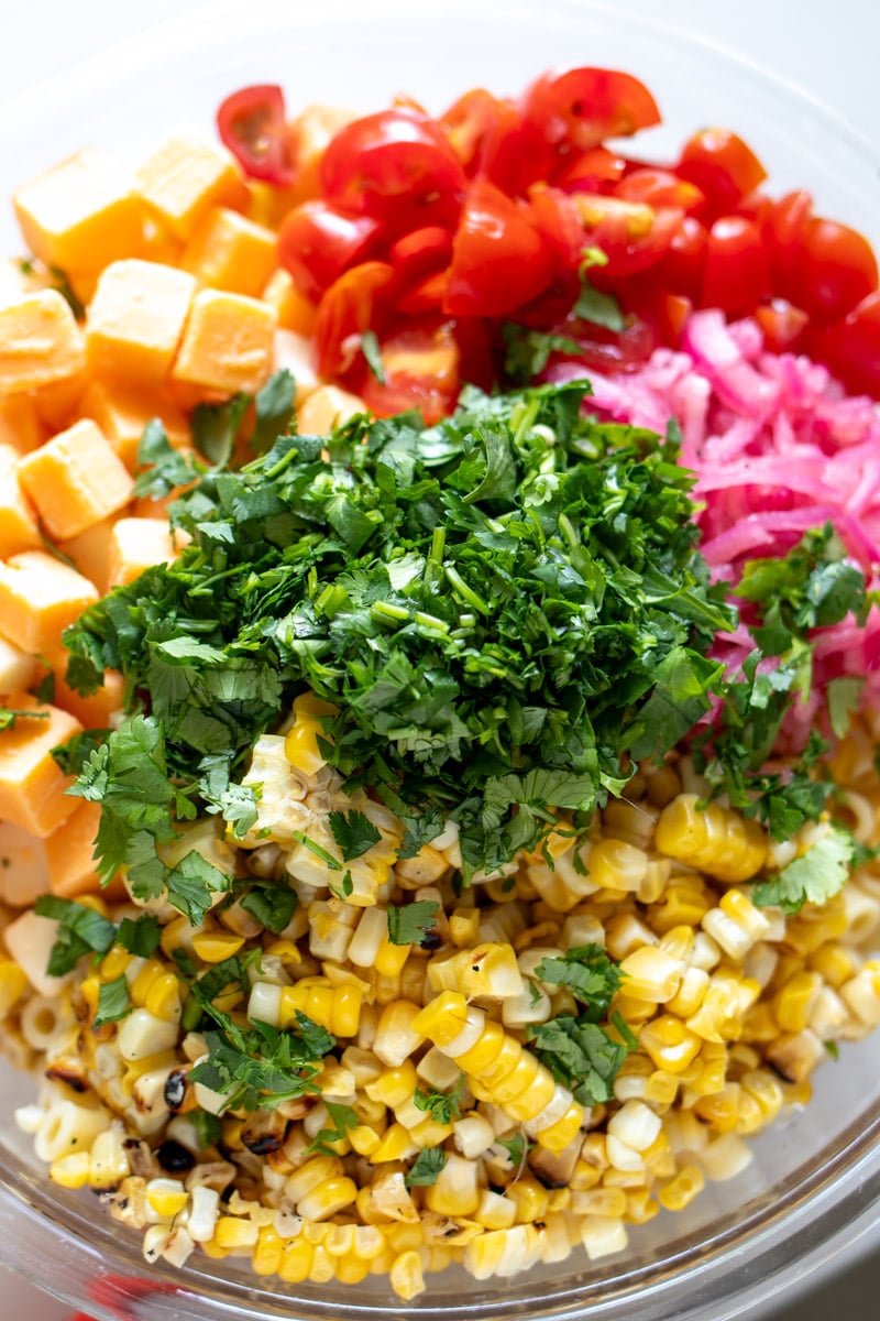 all of the ingredients in mexican street corn pasta salad in a glass bowl.