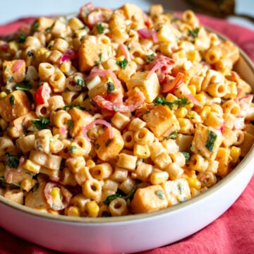 a white bowl full of zesty mexican street corn elote pasta salad on a pink napkin.