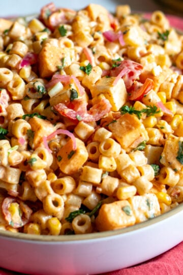 a white bowl full of zesty mexican street corn elote pasta salad on a pink napkin.