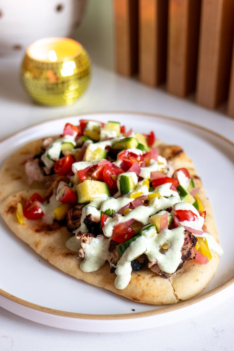 a pita topped with greek yogurt grilled chicken, colorful veggie salad, and greek yogurt sauce. 