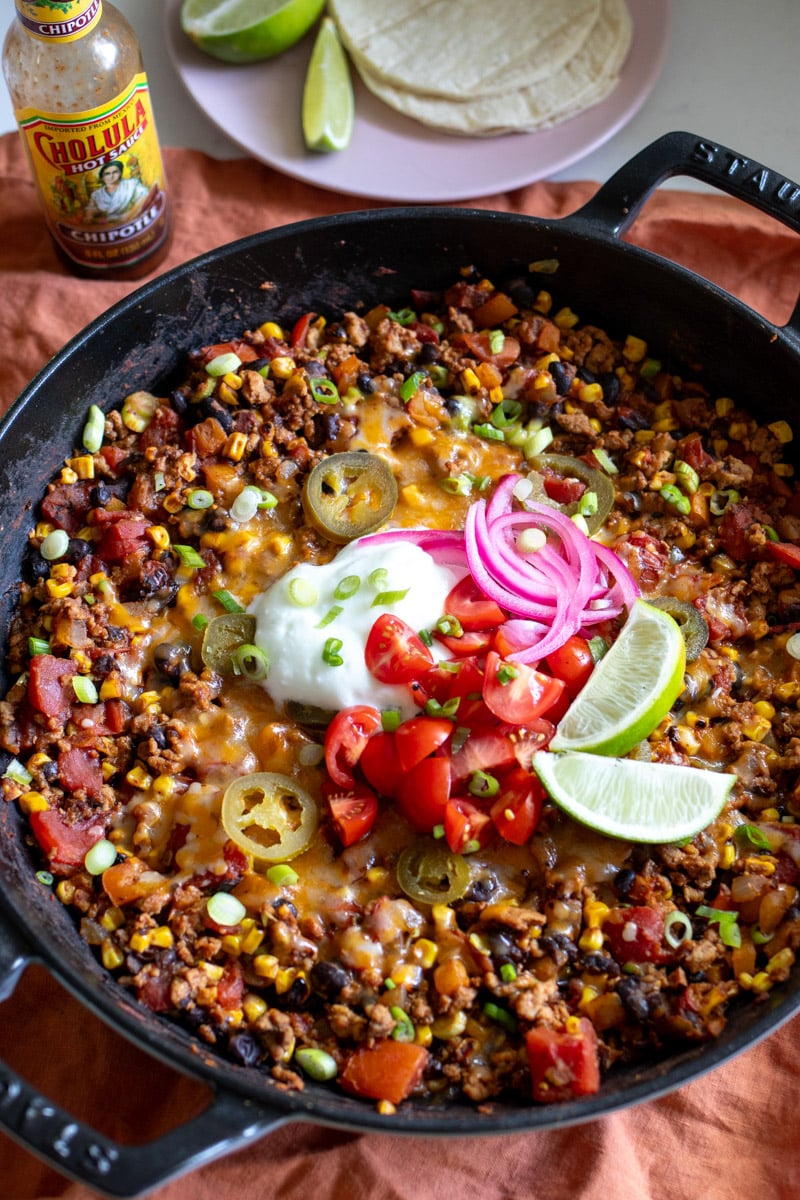 a cast iron skillet full of a healthy taco casserole recipe with colorful toppings on top.