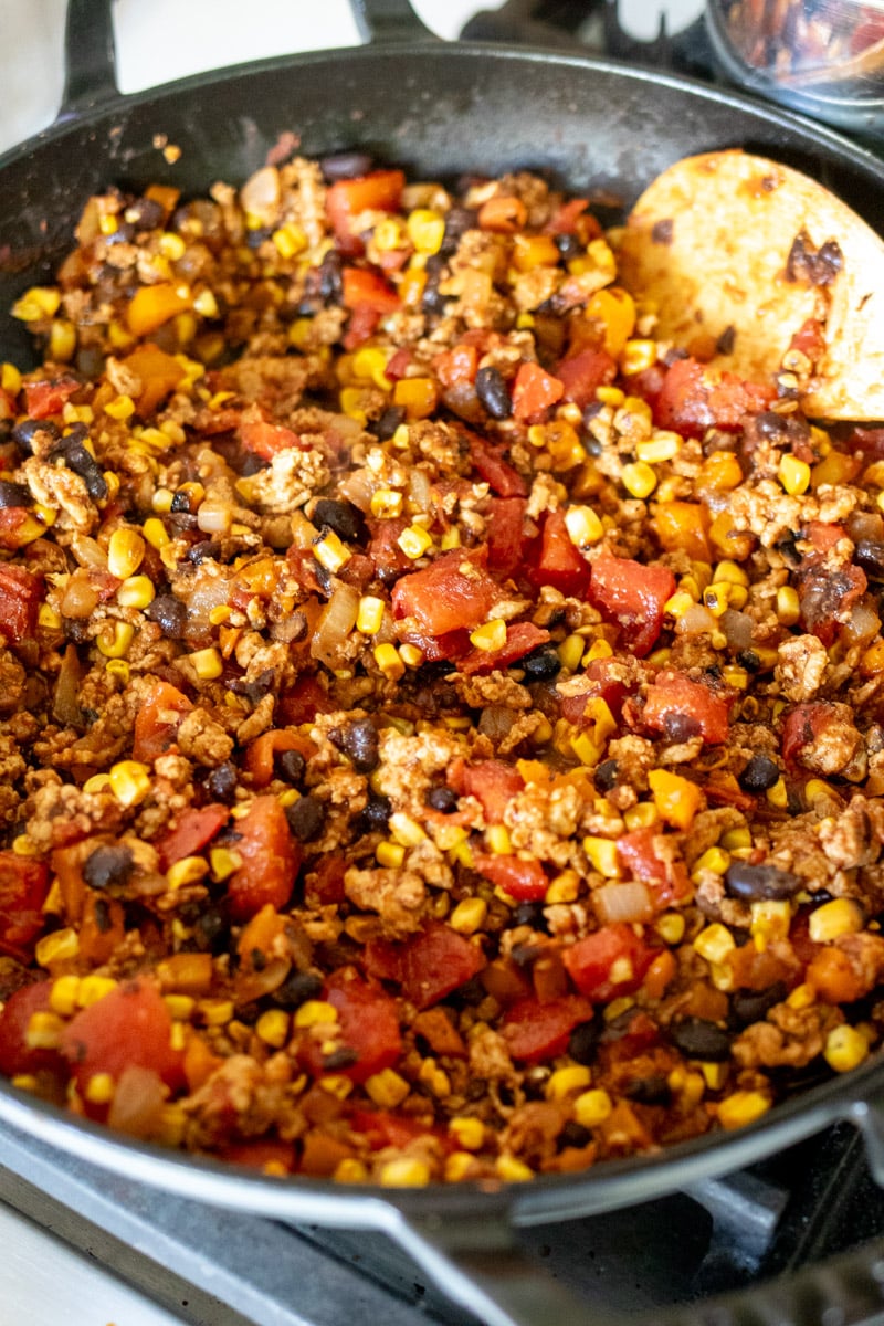 veggies being sauteed with ground chicken in a large cast iron skillet.