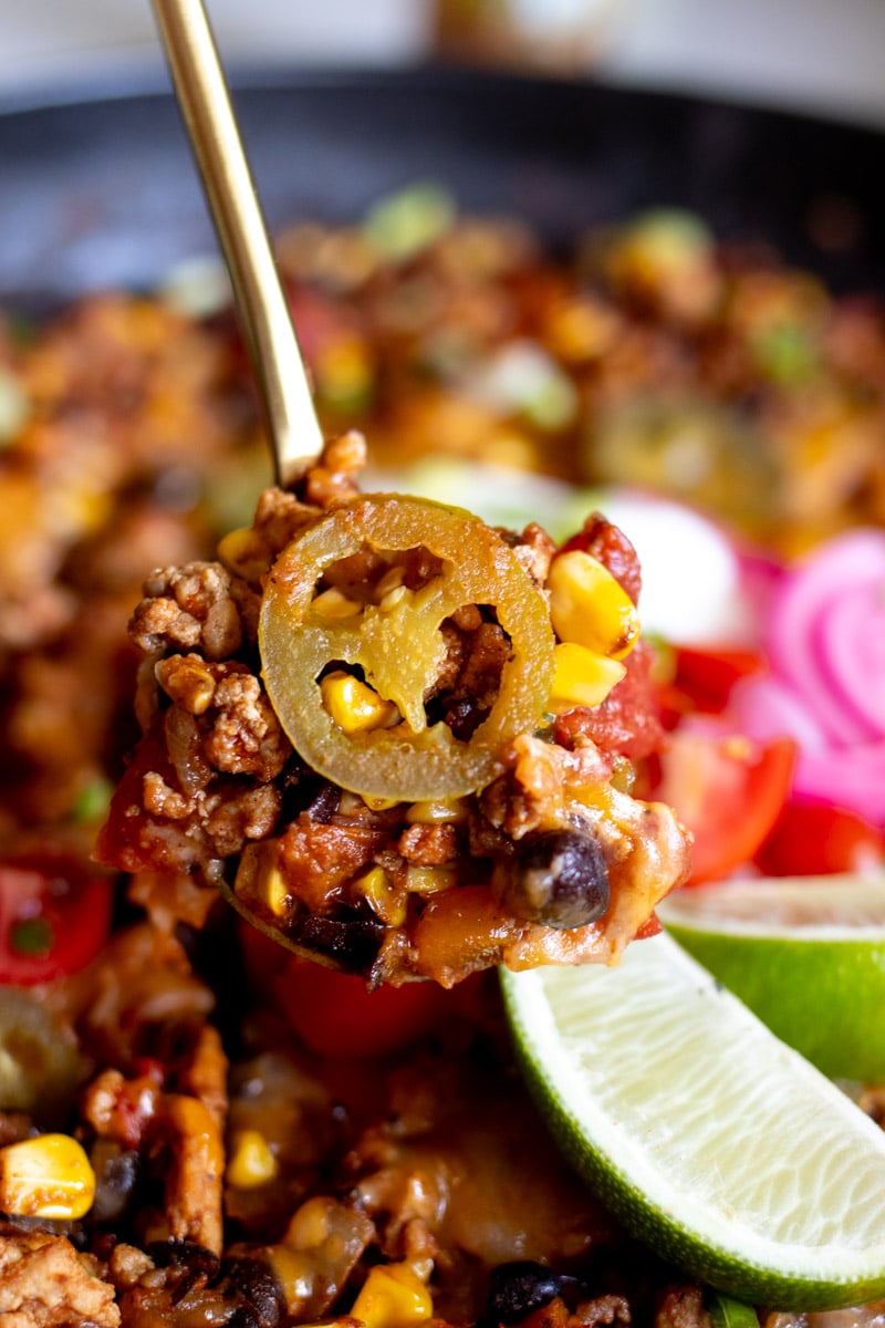 a spoon scooping out some healthy taco casserole with a pickled jalapeno on top.