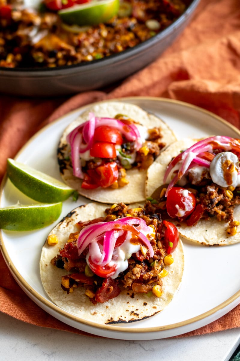 a plate of small tacos stuffed with the healthy taco casserole recipe topped with pink pickled red onions and some lime wedges on the side.