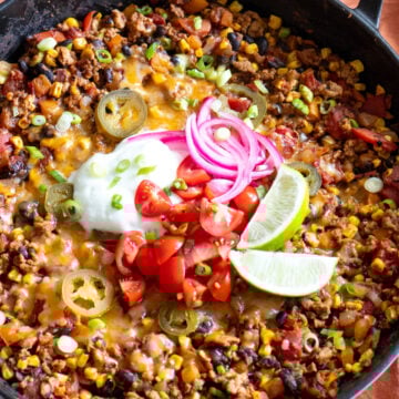 a cast iron skillet full of a healthy taco casserole recipe with colorful toppings on top.