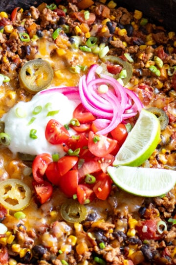 a cast iron skillet full of a healthy taco casserole recipe with colorful toppings on top.