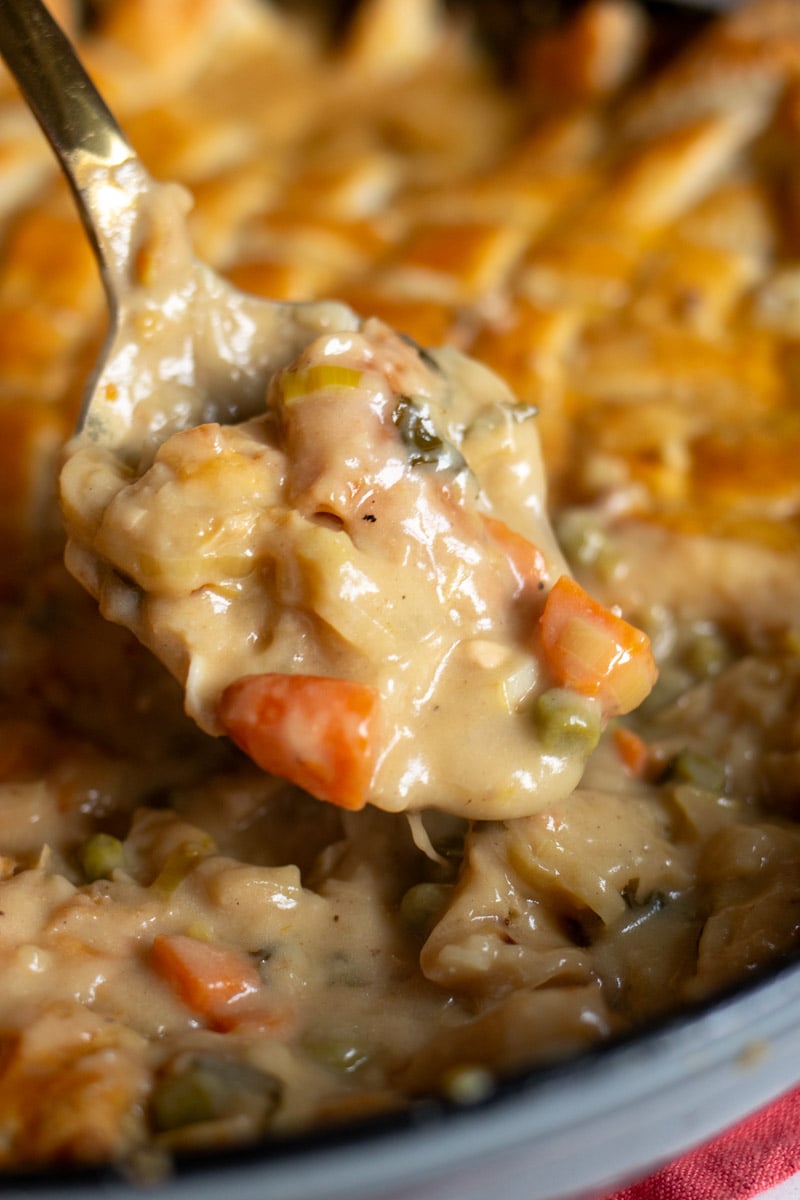 a golden spoon holding a scoop of chicken pot pie. 