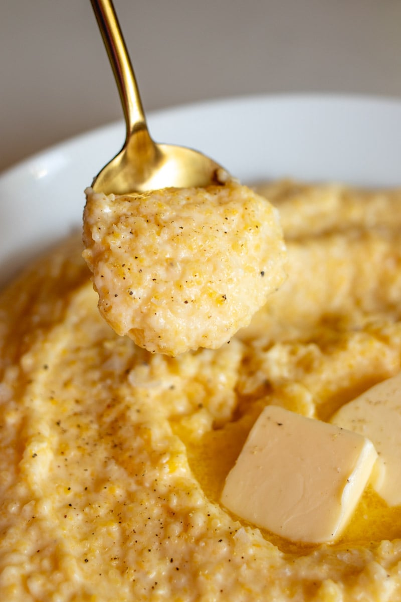 a golden spoon holding a scoop of cheesy polenta. 