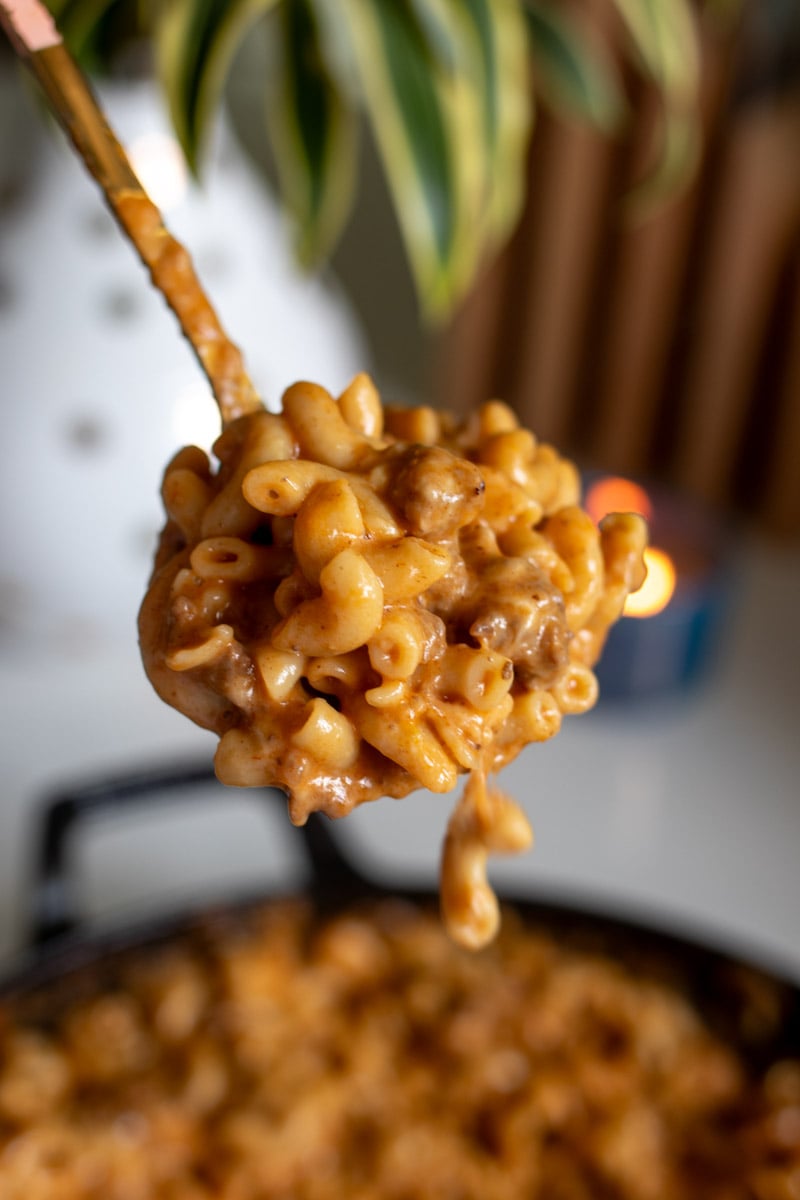 a big spoon of cheeseburger mac and cheese over a white countertop with a plant and a pot in the background.