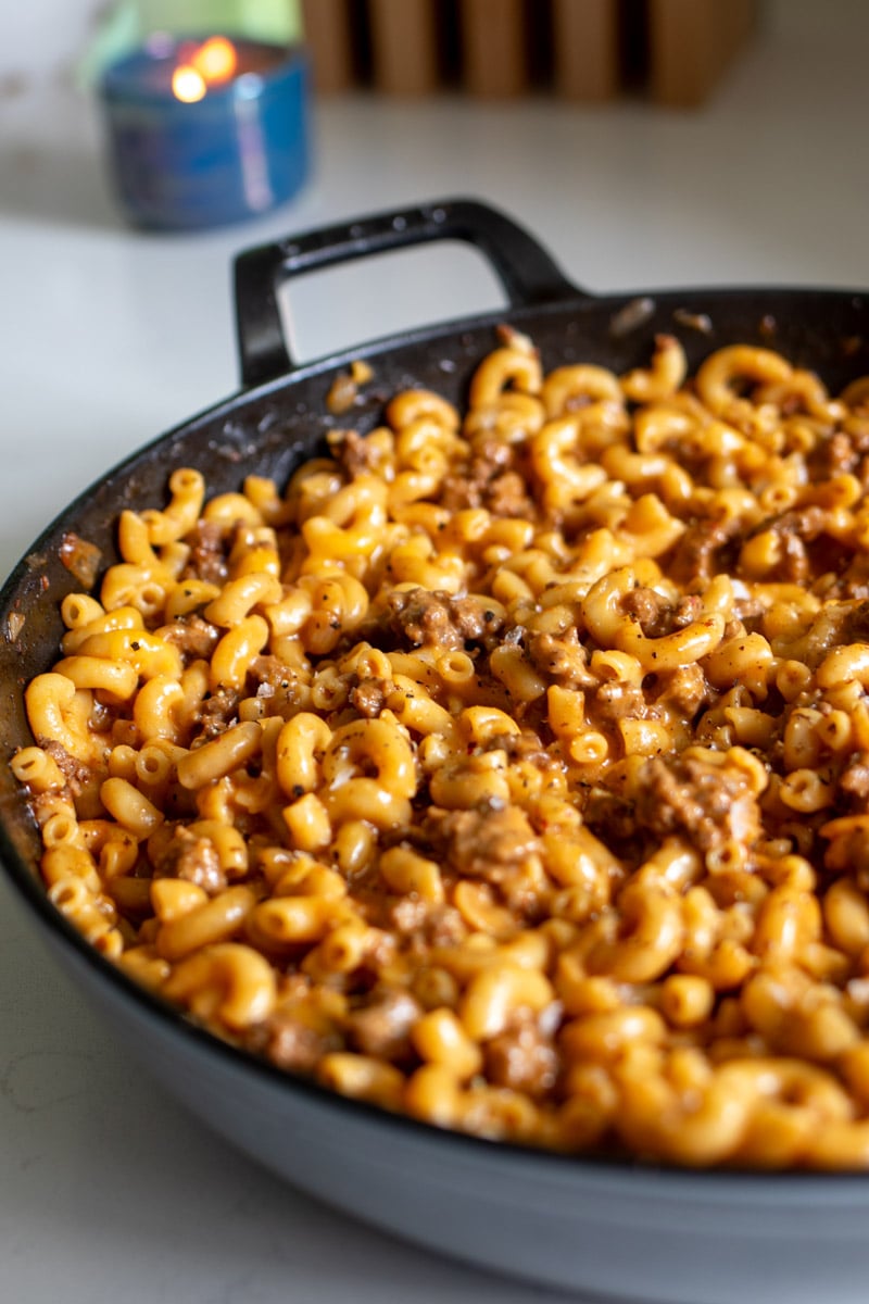 the left side of a big pot of cheeseburger macaroni with a blue candle in the background.