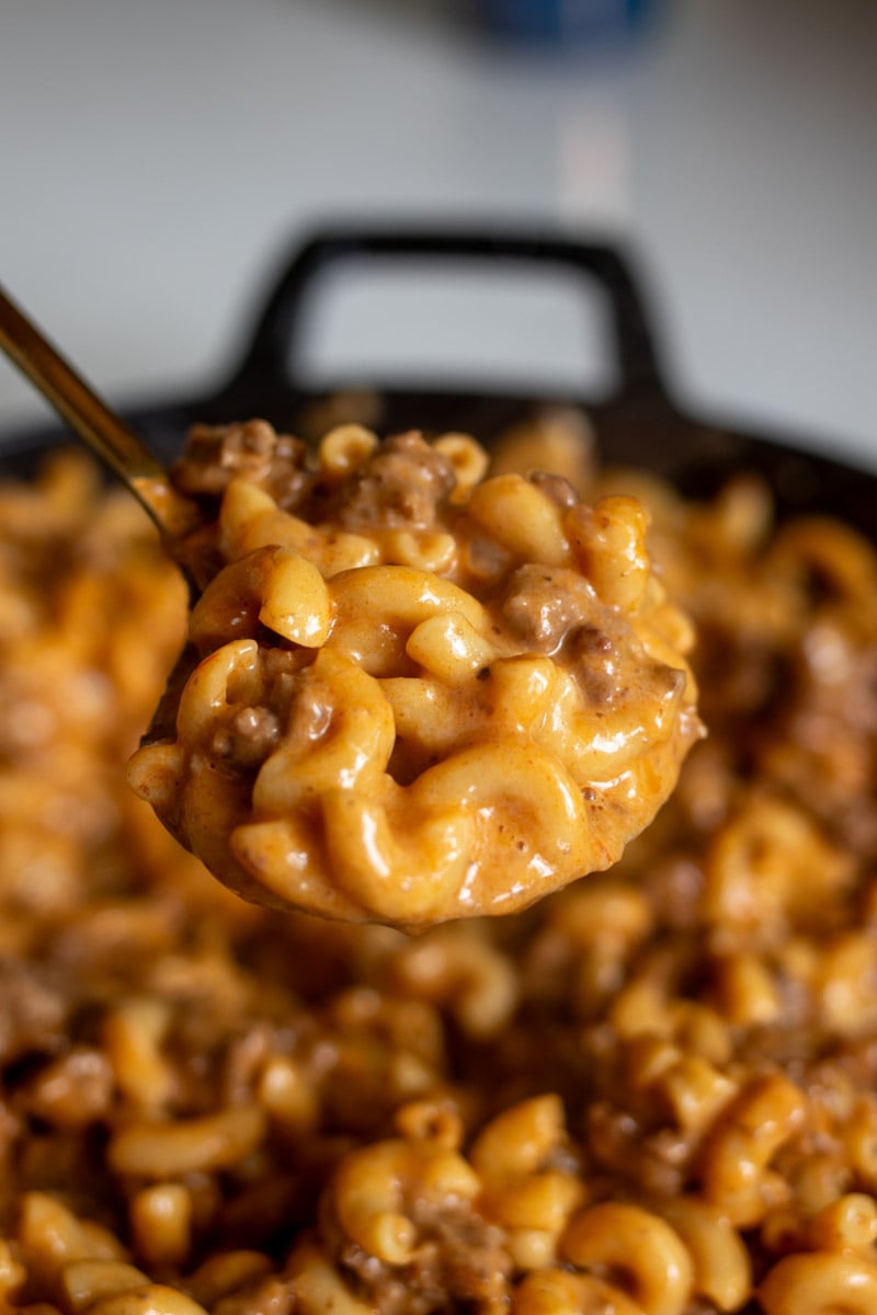 an overhead view of a black braiser full of cream hamburger mac and cheese with a spoon full of it overhead.