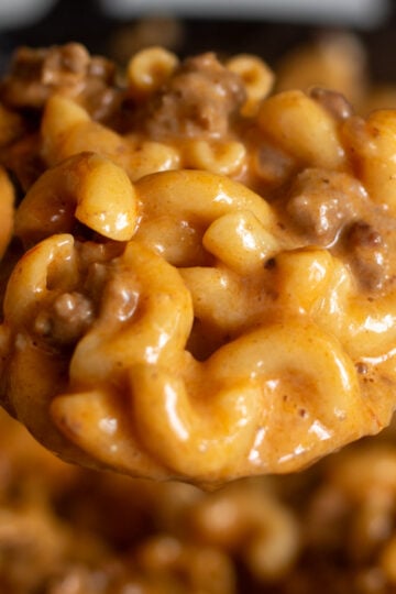 an up close picture of a gooey spoon holding cheeseburger macaroni with bits of ground hamburger meat and a rich cheesy sauce.