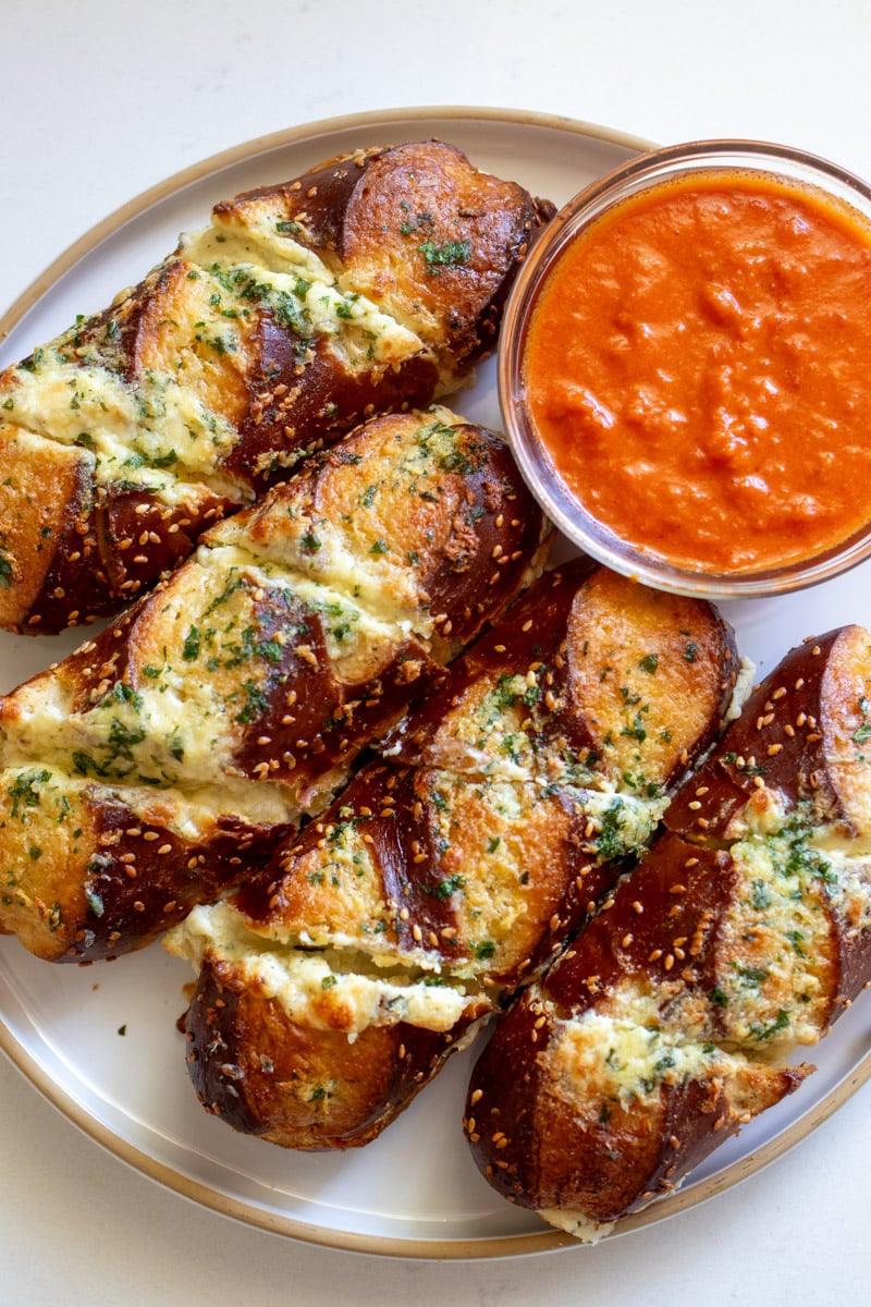 a platter of disneyland's classic cheesy garlic pretzel bread with a small bowl of bright red marinara sauce.