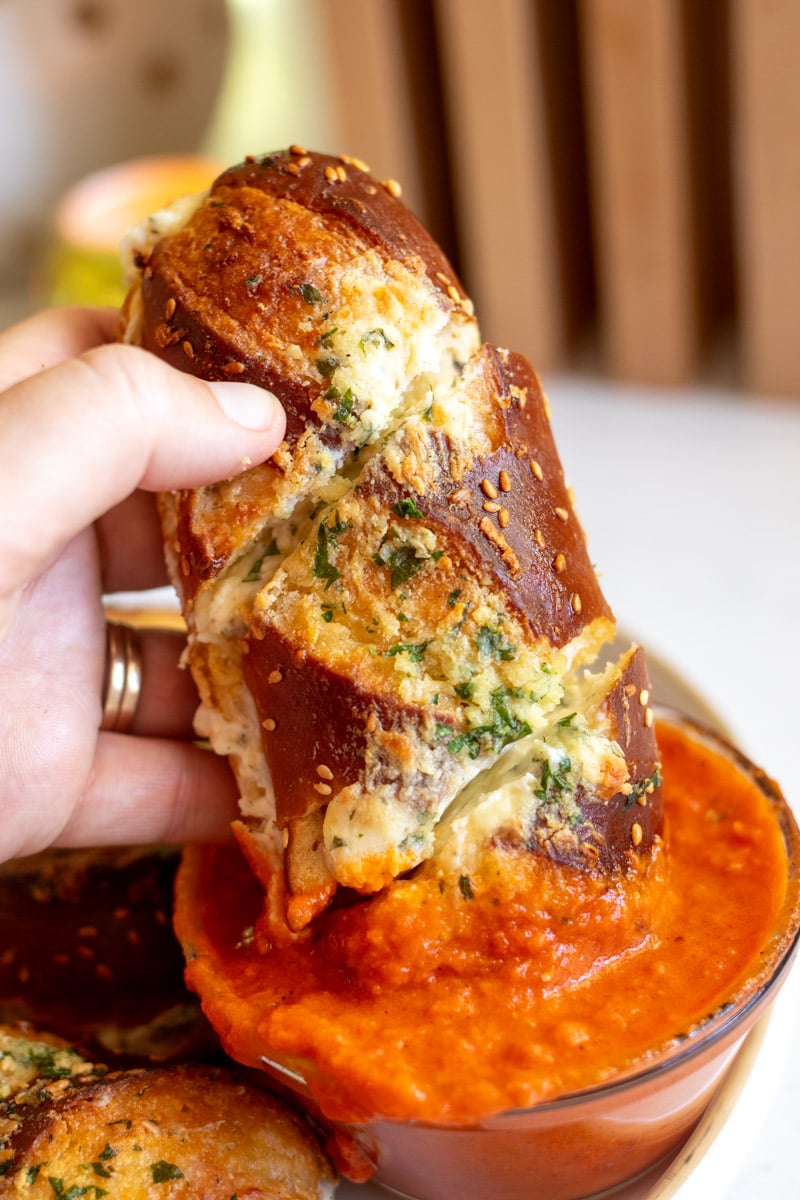 a hand dunking disney's famous cheesy garlic pretzel bread into marinara sauce.