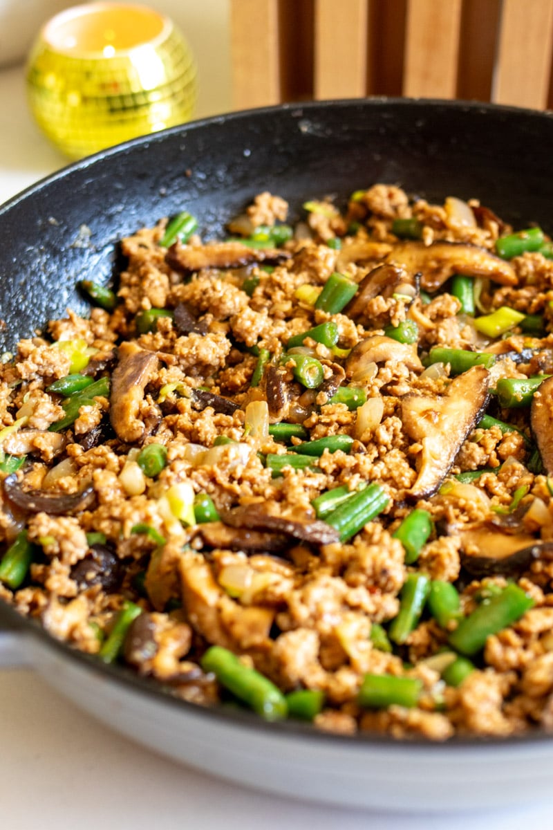 a cast iron full of ground pork stir fry with bits of mushroom and green beans.