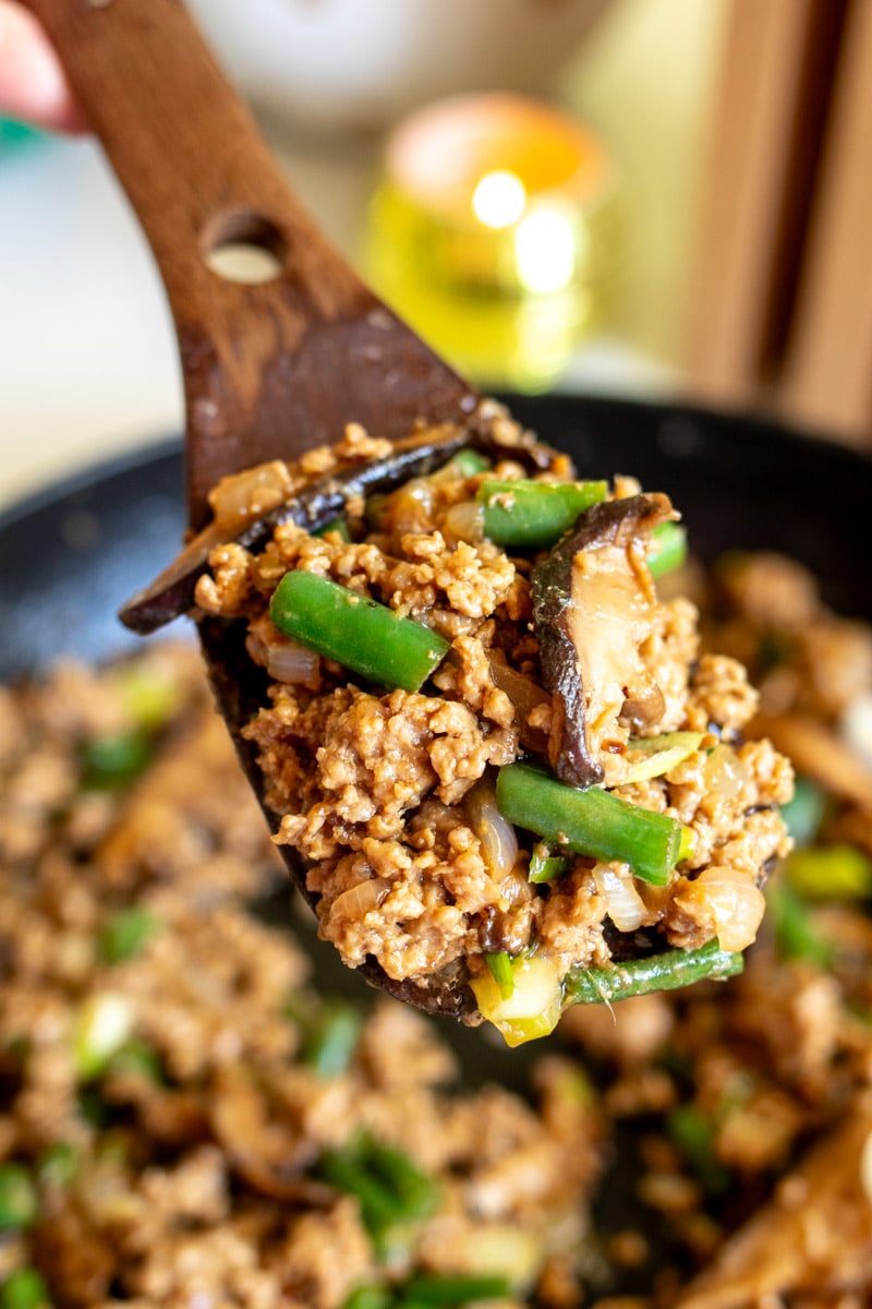 a wooden spoon holding a scoop or ground pork stir fry.